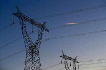 Many high-voltage power towers, silhouetted against the setting sun