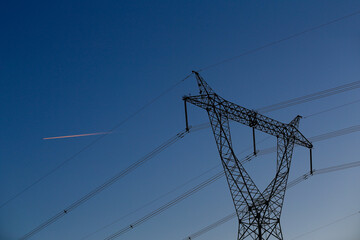 Many high-voltage power towers, silhouetted against the setting sun