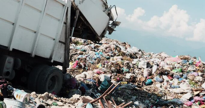 A garbage truck dumping waste at a large landfill under a clear sky
