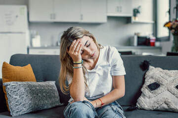 Depressed or tired teen girl feeling stress headache hurt pain sitting alone at home, upset sad...