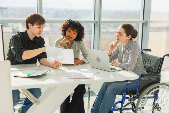 Teamwork brainstorm. Diverse multiracial colleagues woman in chair for people with disability working together. Group of people sitting in creative office discussing business. Young professional team