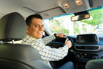 Happy latin man driving a car and smiling for the camera during his morning commute to work