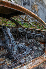 Une carcasse de voiture entièrement brulée et rouillée est stationnée sur le bord d'une route de campagne. Le véhicule est entièrement détruit à l'intérieur et à l'extérieur.