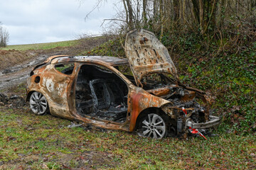 Une carcasse de voiture entièrement brulée et rouillée est stationnée sur le bord d'une route...