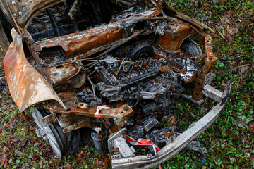 Obraz premium Une carcasse de voiture entièrement brulée et rouillée est stationnée sur le bord d'une route de campagne. Le véhicule est entièrement détruit à l'intérieur et à l'extérieur.