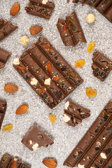 Broken chocolate pieces with nuts and raisins on a stone background top view