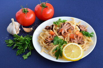 a plate of spaghetti with octopus and a lemon and a tomato on it