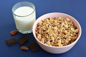 a bowl of granola next to a glass of milk with some almond nuts 