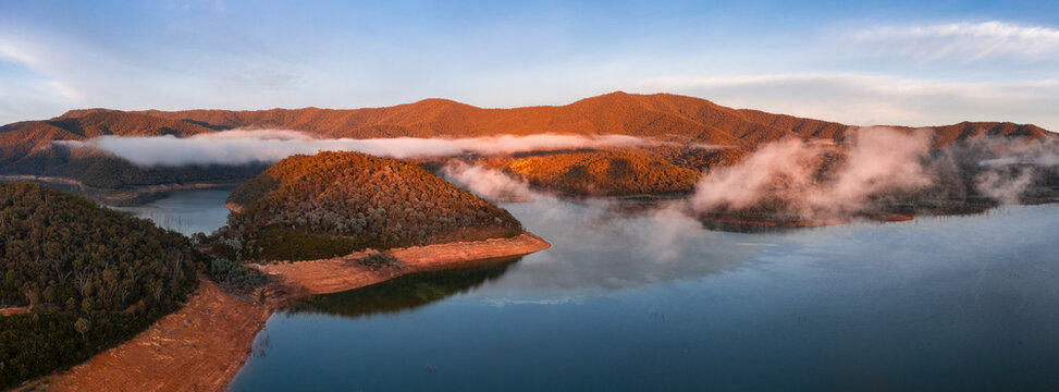 Aerial panorama of early morning light on clouds of fog and hills surrounding a high country lake