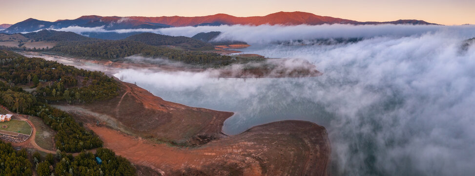 Aerial panorama of early morning light on clouds of fog and hills surrounding a high country lake