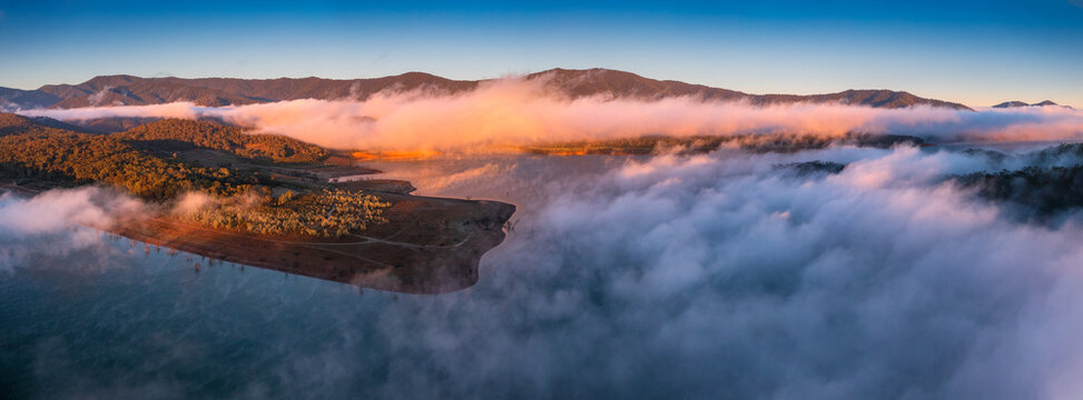 Aerial panorama of early morning light on clouds of fog and hills surrounding a high country lake