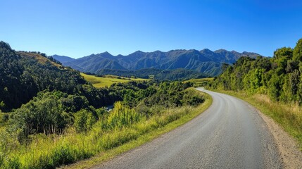 Fototapeta premium Asphalt road meandering through vibrant green countryside, flanked by mountains under a clear blue sky, inviting scenic drive in nature.