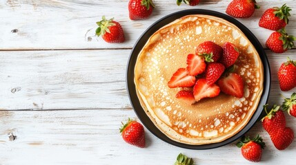 Stack of fluffy pancakes topped with fresh strawberries on a black plate surrounded by strawberries on a rustic white wooden table