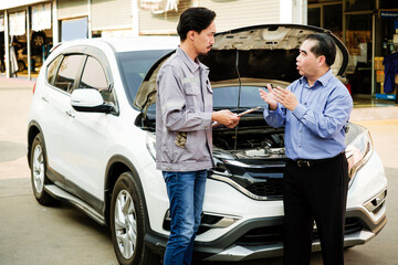 Japanese Mechanic show car checking list for Asian customer with an opened radiator hood car. Focus on mechanic and customer on the right side. Auto car repair service center. Professional service.