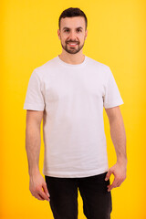 A smiling young man stands in front of a bright yellow background, wearing a plain white t-shirt. His expression is friendly and confident, offering a casual and approachable look.