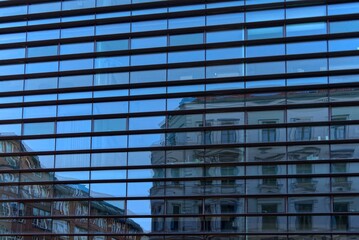 An old facade is reflected in a modern glass facade.