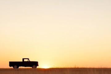 Fototapeta premium A classic truck stands in silhouette against a stunning sunset, with warm hues filling the sky. The peaceful open field creates a tranquil atmosphere, capturing the beauty of dusk