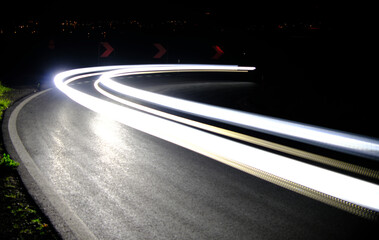 Mesmerizing long exposure shot capturing the light trails of cars speeding through a curvy road at...