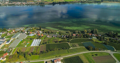 An expansive view from above displaying vineyards and small settlements by a peaceful lake, showcasing the harmonious interaction of nature and human habitation.
