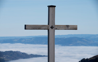 A striking image of a wooden cross standing tall over a fog-covered mountain range, representing spiritual reflection and the majestic beauty of nature above the clouds.