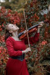 Young woman in red park playing violin in autumn garden © Светлана 