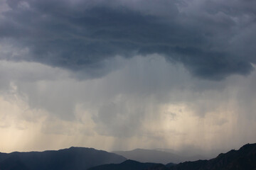 Landscape with dark grey storm rainy sky above black silhouette mountain range. Gloomy grey cloudy sky with copy space for background.