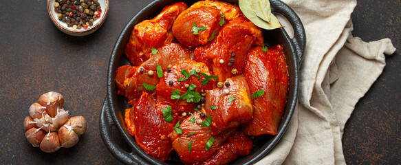 Raw uncooked chopped pieces of meat marinated with seasonings and parsley in black casserole dish top view on dark rustic background. Cooking ragout stew with marinated meat fillet pieces.