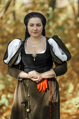 Young woman in medieval dress and cloak standing by tree in forest. Middle Ages