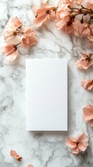 A blank white notepad surrounded by delicate pink flower on a marble background.