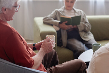 Close up of senior man holding mug with coffee while enjoying time with friends at home or in retirement community copy space