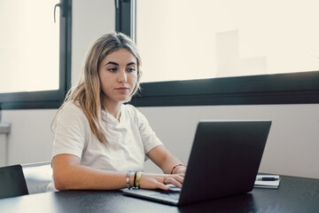 Young student girl sit at table with textbooks and laptop staring aside, studying alone in library,...
