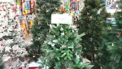 Various artificial Christmas trees with decorated balls and artificial snow are displayed in the shop window.