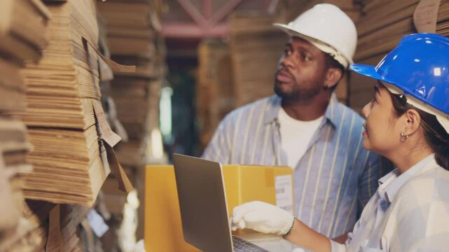 African man worker and asian woman recheck stock at paper factory.
