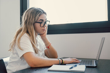 Happy young blonde business woman entrepreneur using computer looking at screen working in internet sit at office desk, smiling millennial female professional employee typing email on laptop workplace