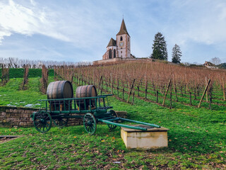 View to Mixed Church of Hunawihr with vineyards and horse cart with wine barrel, Alsace, France