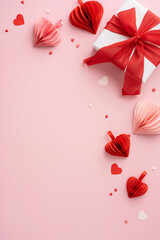 A Valentine's Day themed vertical image featuring a white gift box with a red ribbon surrounded by paper hearts on a pink background. Perfect for romantic occasions and celebrations