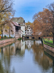 Fototapeta premium Picturesque river view in La Petite France in Strasbourg with half-timbered houses and water reflection, Colourful architecture, canal and blue sky in November, Travel destination, Alsace, France