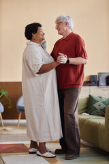 Vertical full length portrait of multiethnic senior couple dancing together enjoying romantic date indoors