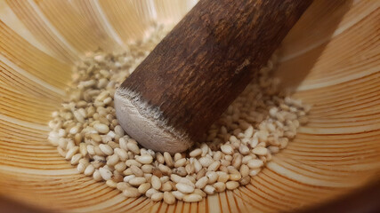 Close up shot of Roasted white sesame seeds in Japanese mortar grinding bowl with wooden grinder ready to serve, Japanese menu, aromatic nuts and seeds, coating ingredient flavor