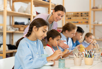 Teenage girl paints a ceramic glass made for a master class with a brush. Children make pottery at...