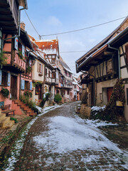 Charming, colorful, snowy cobblestone street with half-timbered houses in snow and colorful facades in Eguisheim, France's most beautiful village, Alsace region, France Travel destination in November