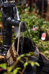 Stream of water from an ancient hydrant flows into a wooden bucket suspended on a rope