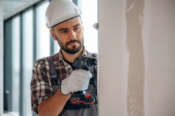 Drilling the wall. A man is renovating an unfinished room