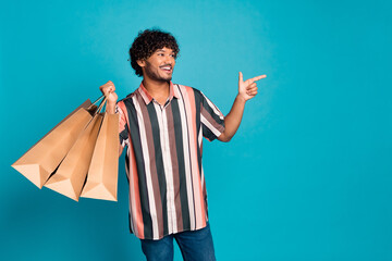Photo of nice young man hold bags direct finger emoty space wear shirt isolated on teal color...