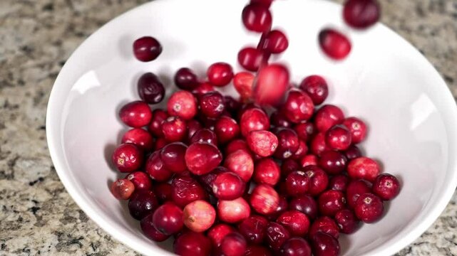 Dropping fresh cranberries into a white bowl on a granite countertop in slow motion