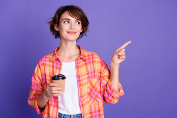 Portrait of pretty young lady point finger empty space coffee cup wear shirt isolated on purple...