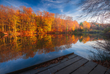 Sunset over the fishing pier. Autumn colorful foliage over lake with beautiful woods in red and yellow color. Bakony Forest and Mountain, Pisztrangos Lake, Hungary. Long exposure shot.