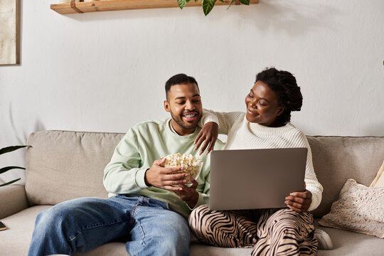 A joyful couple shares warm moments while watching a movie at home, wrapped in cozy sweaters.