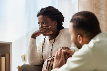 African American man holding hand of his upset girlfriend in their cozy living room