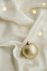 Gold Christmas Ornament on Soft White Fabric. Christmas decoration featuring a glittering golden bauble resting on a smooth white fabric background with soft, warm fairy lights, minimalism and winter-